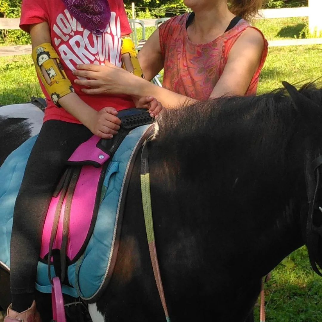 Séance d’hippothérapie : enfant sur un poney accompagné par la kinésithérapeute